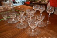 Photo shows 6 dessert glasses each with a matching crystal saucer, arranged on a table with various other glasses in the background.