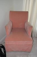 Front view of a pink upholstered armchair with cushioned seat and armrests, showing fabric wear.