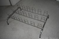 Side angle view of a silver metal wire shoe rack showing three rows of wire slots for shoe placement and curved supporting legs.