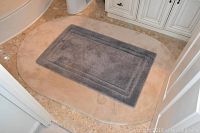 Beige oval bathroom mat with smaller gray rectangular mat placed on top, shown on bathroom floor.
