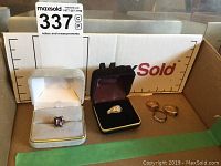 Five rings displayed in box: amethyst ring in white box, gold-filled engagement ring in maroon box, and three gold bands