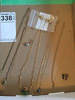 Overview of all gold chains with pendants, assorted earrings in plastic bag, and butterfly pin placed on cardboard.