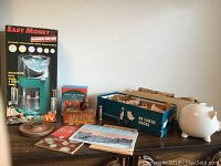 Easy Money II motorized coin bank in original box, white ceramic piggy bank, a box of rolled coin wrappers, vintage coin books and pamphlets on a wooden surface.