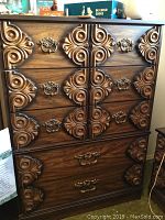 Front view of vintage wooden dresser showing all 5 drawers with ornate carved wooden designs and decorative metal handles.