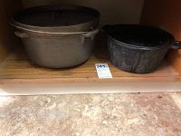 Two cast iron Dutch ovens side by side on shelf, showing size difference and lids in place.