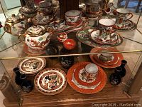 Wide view showing full collection of Asian dishware including teapot, teacups, plates, and vases on glass shelves.