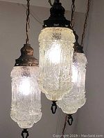 Close-up of the three glass globes of the vintage swag lamp illuminated, showing intricate embossed patterns on the glass.