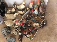 Overview photo showing a collection of ceramic and resin garden gnomes and animals, including geese, turtles, and multiple gnomes in various poses and color schemes.