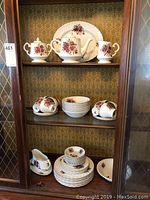 Full view of china cabinet shelf displaying teapot, sugar bowl, creamer, cups, saucers, and plates with Rosewood floral pattern