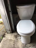 Full view of white American Standard toilet showing bowl and tank, placed on concrete floor near garage door.