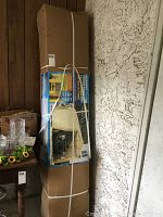 Tall sealed carton leaning against wall showing bundled boxed components.
