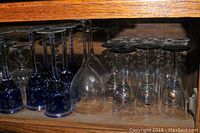 Two shelves of mixed stemmed glasses including clear crystal, blue patterned glasses, and gold metal stemmed cups.