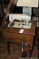 Photo showing vintage Sears Kenmore sewing machine integrated into a wooden sewing table with drawers and fold-down compartment.
