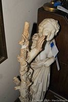 Full side view of marble statue showing woman with ornate carved tree branch wrapped around her arm with detailed leaves and flowers.