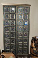 Front view of both metal embossed door panels leaning against wall with barrel nearby.