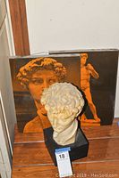 Photo showing the David sculpture bust on a black base alongside two prints featuring the statue in orange tone, including a close-up and full view.