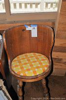 Front view of the vintage child's wooden chair showing rounded back and seat cushion.