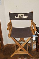 Full view of wooden directors chair with fabric seat and backrest marked Dom Salinaro.
