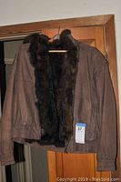 Brown leather jacket with mink fur lining visible, hanging on wooden hanger.