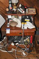 Photo of vintage wooden nightstand with clutter on top and inside. Shows drawer closed and open, revealing condition and size.