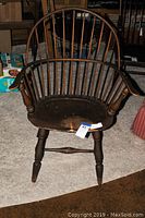 Full view of vintage wooden Windsor chair with sack back, armrests and turned legs.