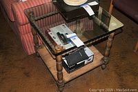 Full view of square coffee table with clear glass top and wooden spindle legs, lower shelf visible with some items on it
