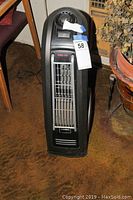 Front view of black Lasko standup fan showing vertical grille and control panel on top.