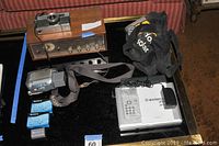 Vintage Sony AM FM radio with wood casing, Olympus Quic Matic EEM camera, Sony Handycam with Carl Zeiss lens, Sony DVC tapes, and battery pack on black surface.