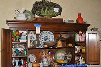 Wide view of wooden cabinet filled with assortment of memorabilia including pottery, plates, figurines, and decorative items.