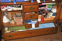 Wide shot showing opened drawers and shelves with folded table linens, ceramic soup bowls stacked in top shelf, candles, gift bags, and a wicker basket.