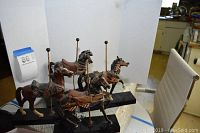 Four carousel horse figurines displayed together on black bases with brass poles in front of a white backdrop and a height measurement card.