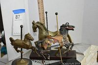 Photo showing three brass carousel horse figurines, two mounted on wooden bases with twisted poles, one smaller on round base.