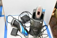 Philips and Panasonic wet/dry electric shavers with their respective power adapters and charging dock for Panasonic.