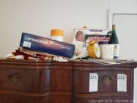 Wide shot of memorabilia lot displayed on a wooden dresser featuring various items including a folded jersey, framed photos, a clock and a decorative bottle.