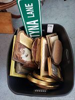 Top-down view of multiple wooden frames and a green street sign labeled 'STYNA LANE' in a black plastic bucket.