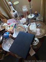 Photo showing various glassware items including bowls, jars, Pyrex dishes with lids, a butter dish, and other decorative pieces arranged on a table.