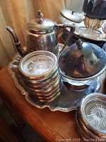 Silver plated tea pot, bowls with lids, glass coasters with silver rims, creamer, and tray shown together on table