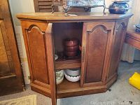 Full view of wooden cabinet with double doors open revealing interior shelves with bowls inside.