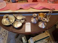 Full view of lot items including sterling silver candlestick holders, cups, a tall glass, pewter candle stick holder, and small bowls.