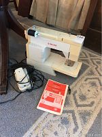 Singer Stylist sewing machine on blue patterned carpet with attached foot pedal and power cord, instruction manual placed in front.