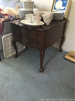 Full front and side view of the wooden side table with crockery on top showing overall shape, color, and details.