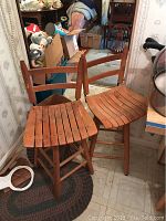 Two vintage wooden swivel counter stools positioned side by side showing slatted wooden seats, backs, and legs with visible wear and discoloration.