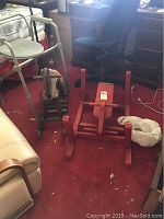 Photo showing red wooden rocking horse upside down or disassembled on carpet with white walker and office chair nearby