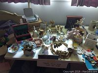 Photo of table featuring Noritake dish, plush cat decor, carousel horse figurines, and assorted collectibles.