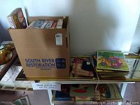 Wide view of box containing various vintage board games and children's puzzles arranged on a glass tabletop.