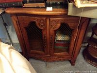 Photo showing entire wooden cabinet with wire mesh on doors and sides, carved details and metal handles.