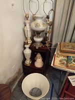 Six lamps grouped together on a small table and floor corner, various styles and ceramic bases, one cream linen shade seen on the floor.