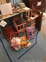 Full view of wooden doll furniture assortment: high chair, crib, bed, ironing board with dolls and a book on the side.