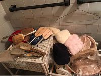 Vintage girls hats, hand muffs, and vanity accessories arranged on white wicker furniture showing variety of hats and faux fur muffs alongside vanity items