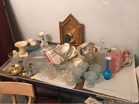 Table showing wide assortment of glassware, porcelain dishes, vases, candle holders, and framed art, indicating a mixed lot of Nippon and Noritake china and decorative items.